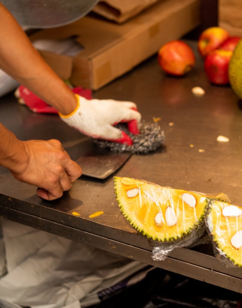 Hands slicing jackfruit in a vibrant New York market stall, showcasing fresh produce.
