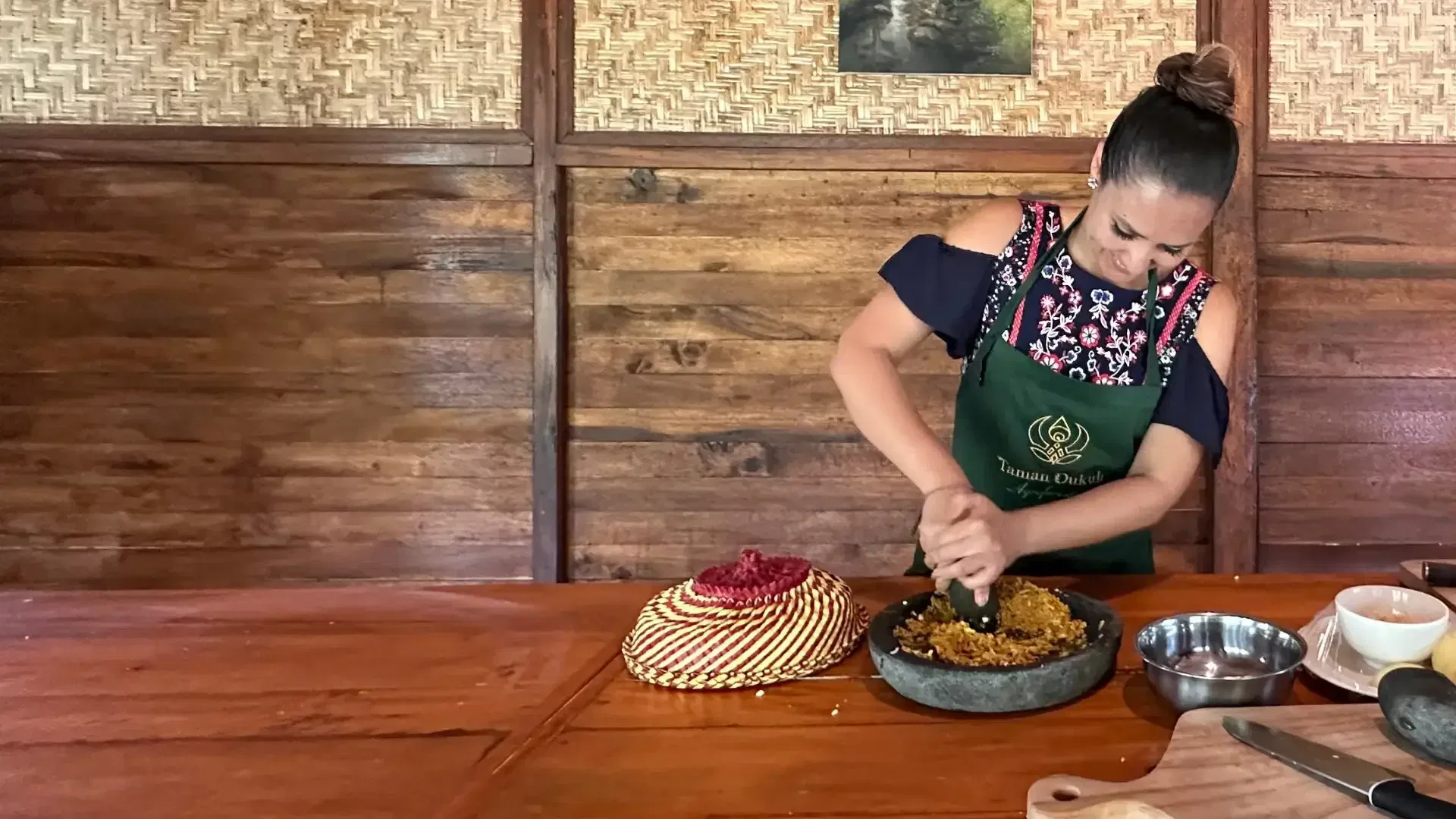 A woman grinding peanut sauce using a traditional mortar and pestle during a Balinese cooking class.