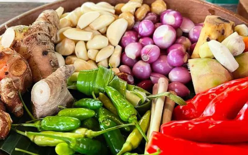 A collection of essential Balinese spices and fresh ingredients like chilies, galangal, and turmeric, sourced from an Ubud organic farm.
